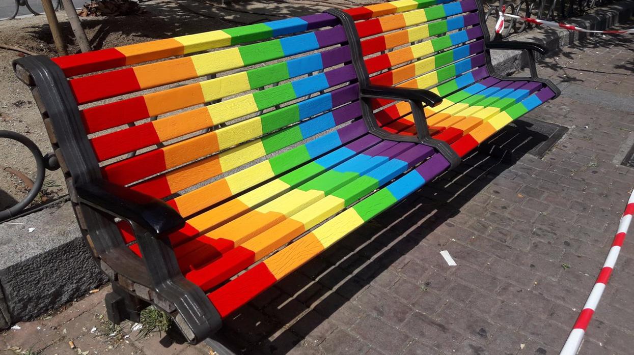 Un par de bancos pintados con los colores representativos del Orgullo frente a la Junta Municipal de Puente de Vallecas