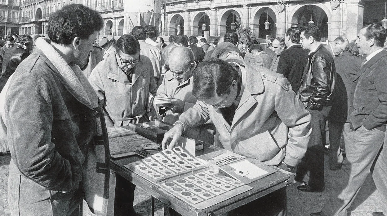 Varios hombres analizan una colección de monedas en la Plaza Mayor