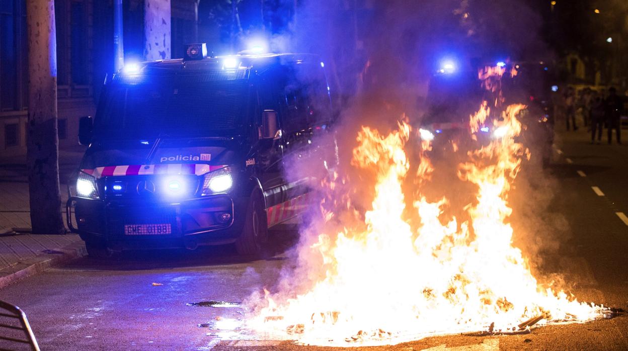 Un furgón de los Mossos d'Esquadra pasa junto al fuego durante los altercados al finalizar la movilización por el aniversario del 1-O