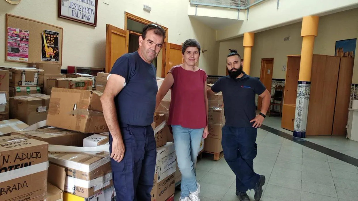 La bibliotecaria, María José Olivares, con dos voluntarios, posa ante decenas de cajas con libros donados