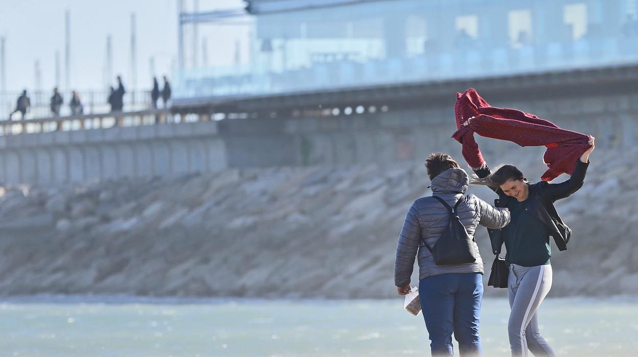 Dos personas se protegen de las fuertes rachas de viento en la playa de Las Arenas de Valencia