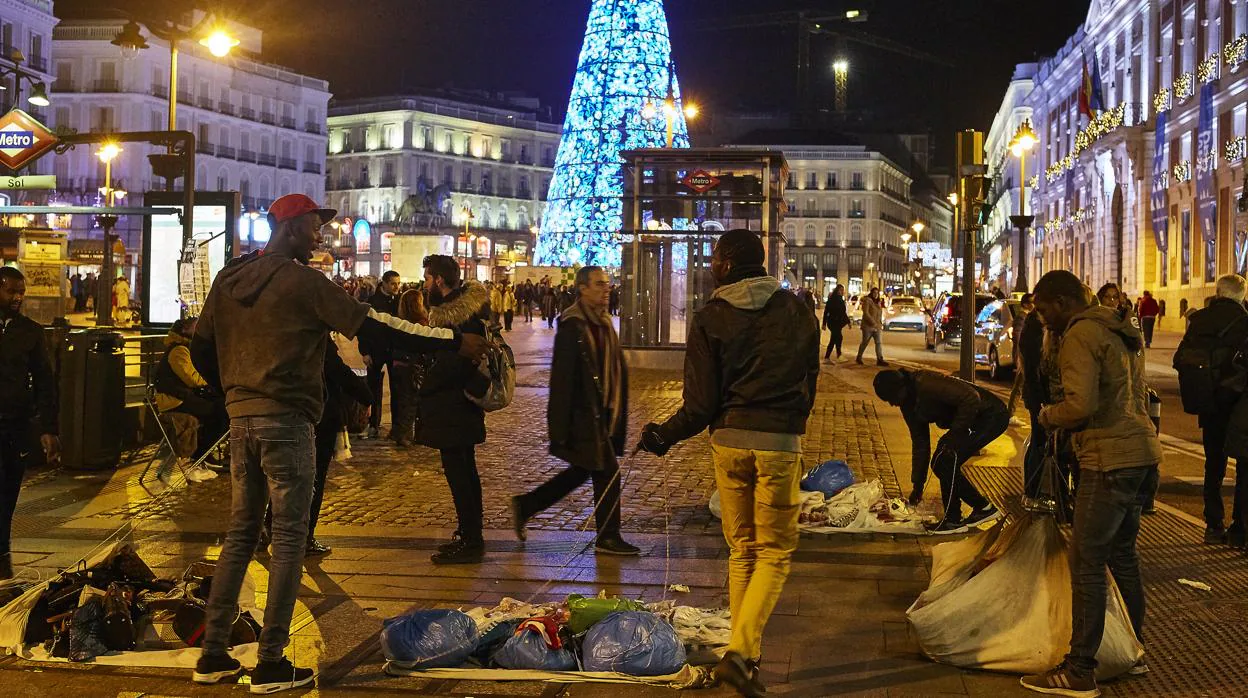 Un grupo de manteros, de noche, vende sus productos en la Puerta del Sol