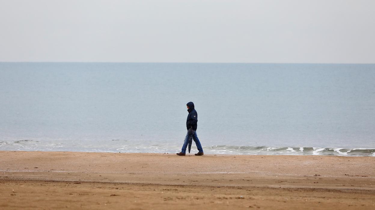 Un hombre se protege de la lluvia en una playa de Valencia