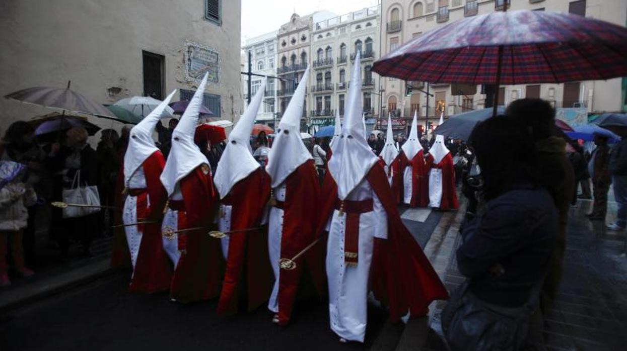 Una procesión en Valencia con el público protegiéndose de la lluvia con paraguas