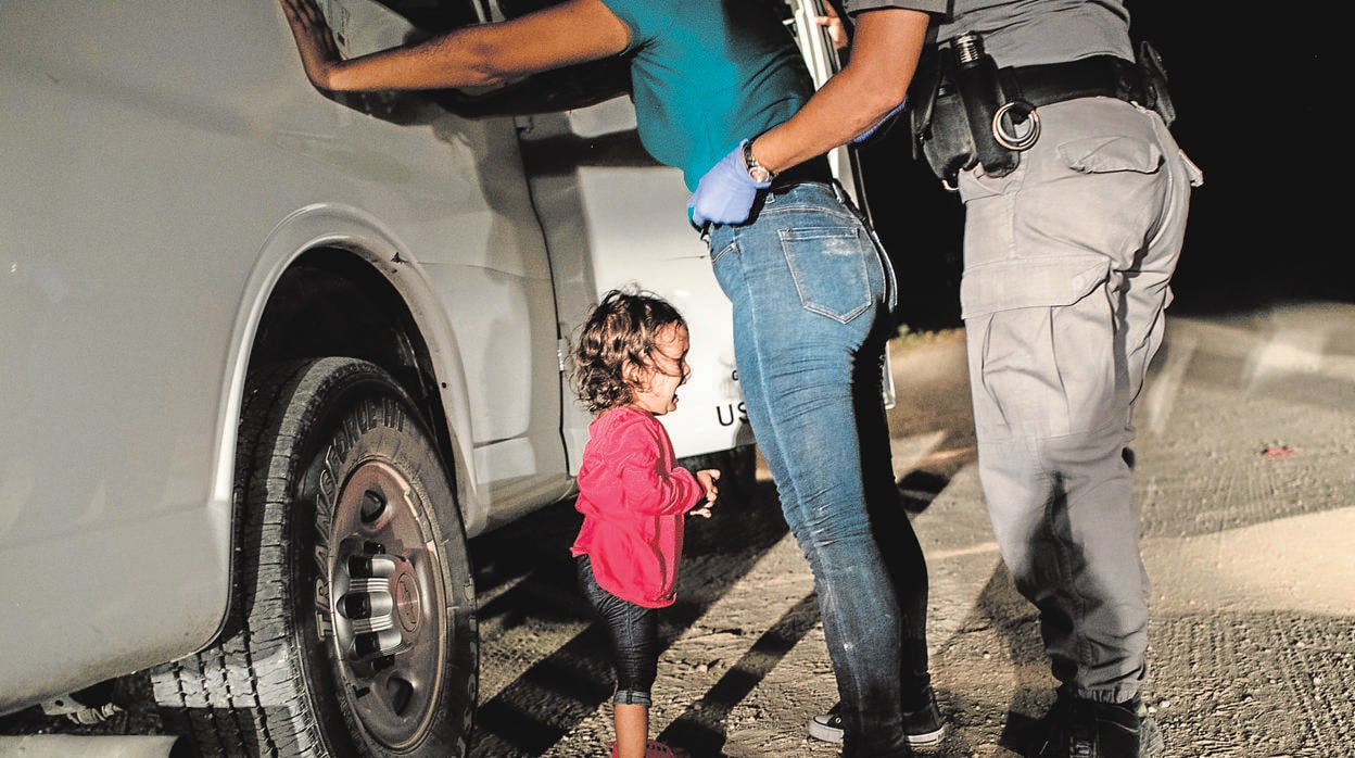 La niña Yanelaa, de Honduras, llora mientras su madre es cacheada por un policía de fronteras