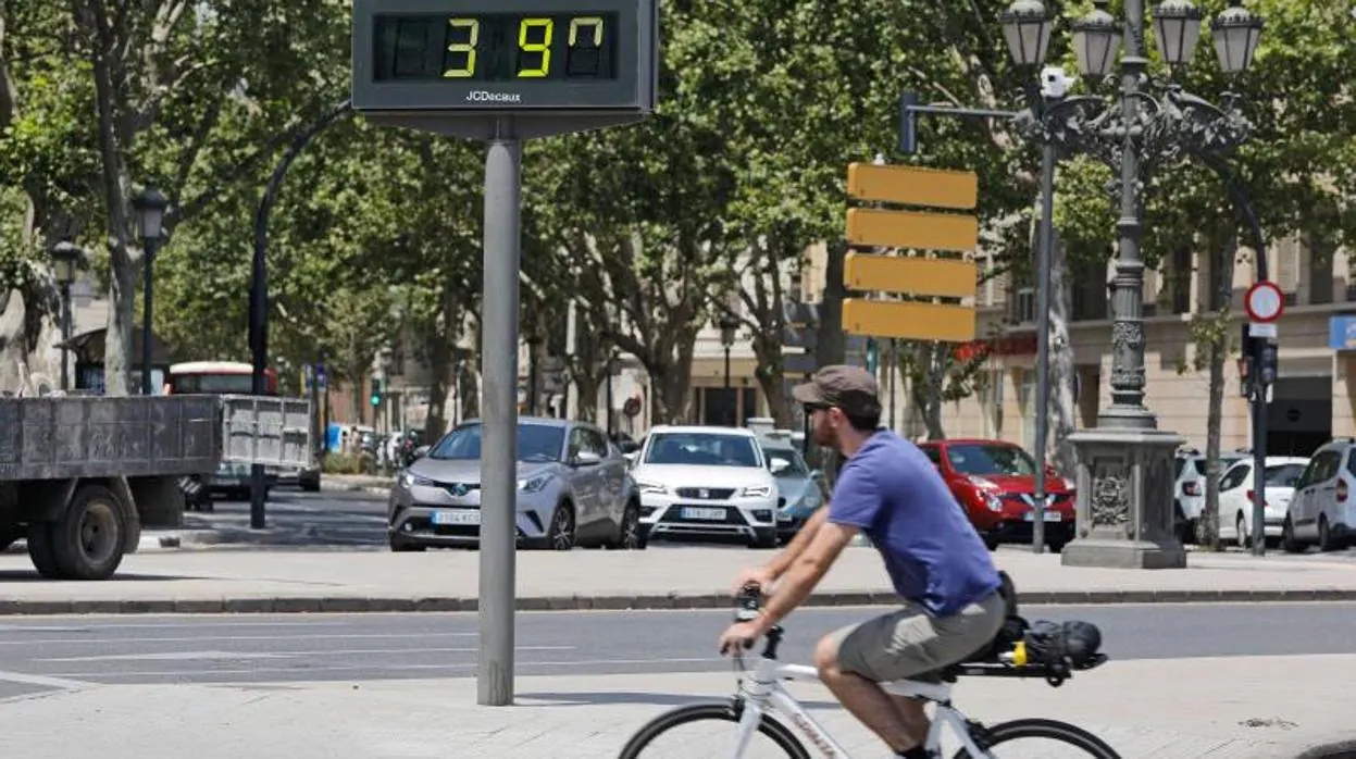 Un ciclista pasa junto a un termómetro que marca 39 grados en la ciudad de Valencia