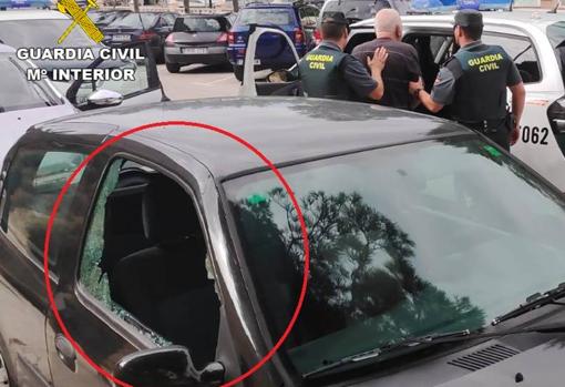 El caco custodiado por dos agentes y uno de los coches que intentó robar, con la ventanilla reventada