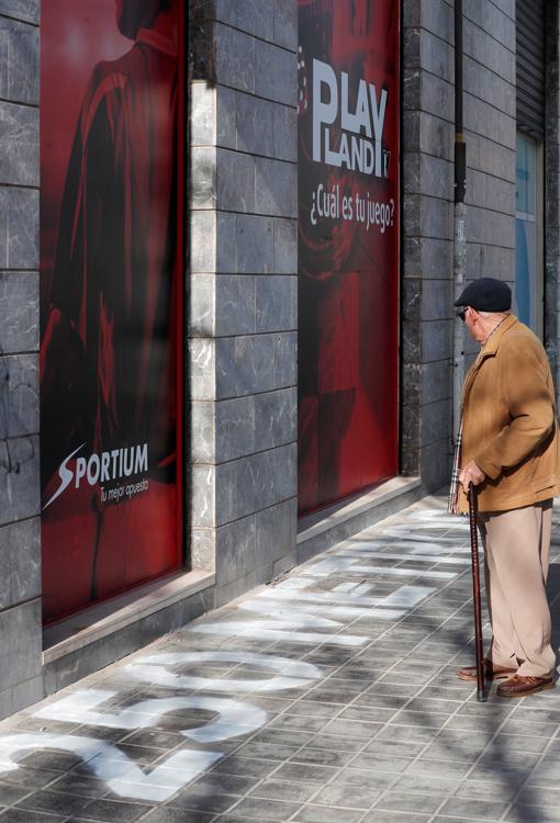 Imagen de n señor contemplando la pintada de «250 metros» ante una de las casa de apuestas señalizadas por su distancia hasta el centro educativo más próximo en Valencia