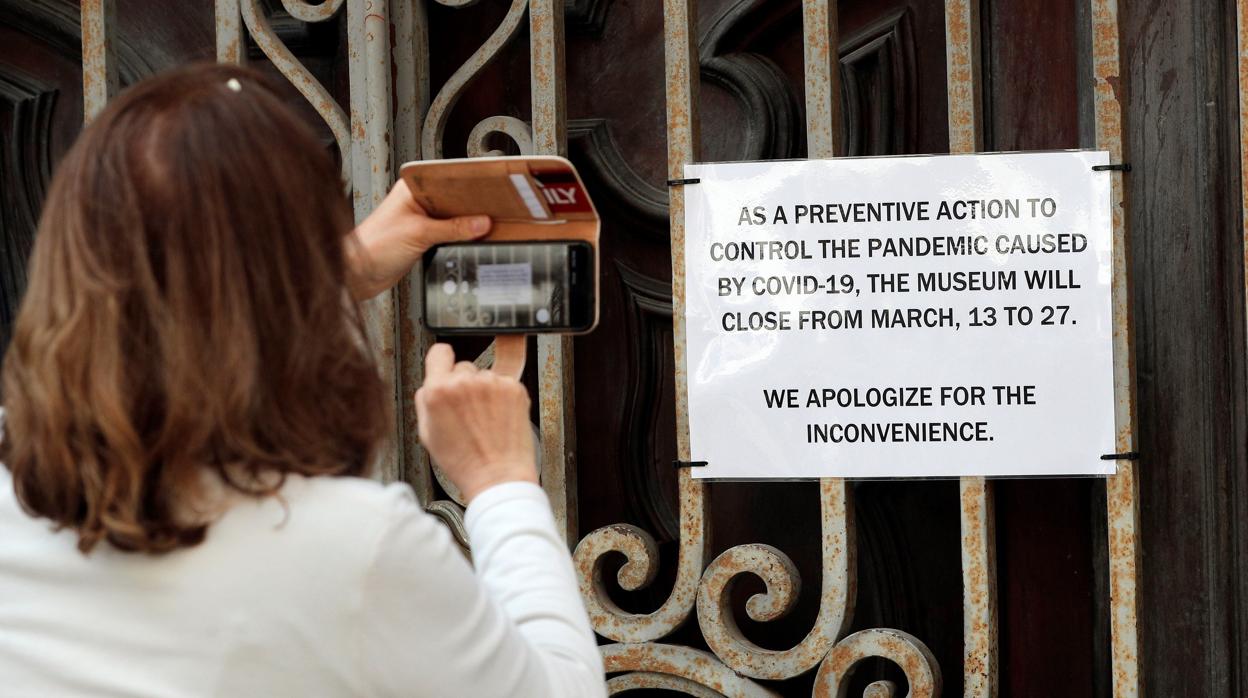 Imagen de una mujer fotografiando un cartel en inglés que anuncia el cierre del Museo Nacional de Cerámica