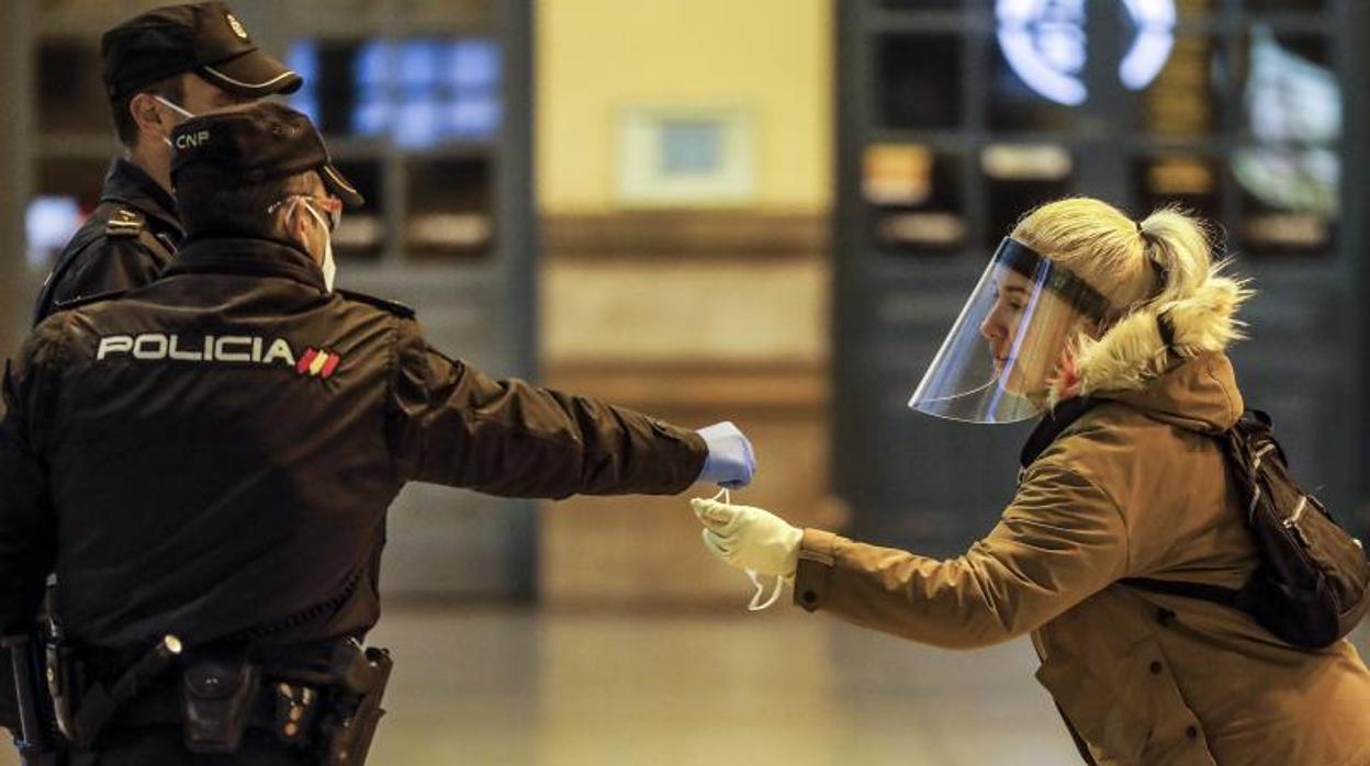 Dos agentes de la Policía Nacional entregan una mascarilla a una mujer en Valencia