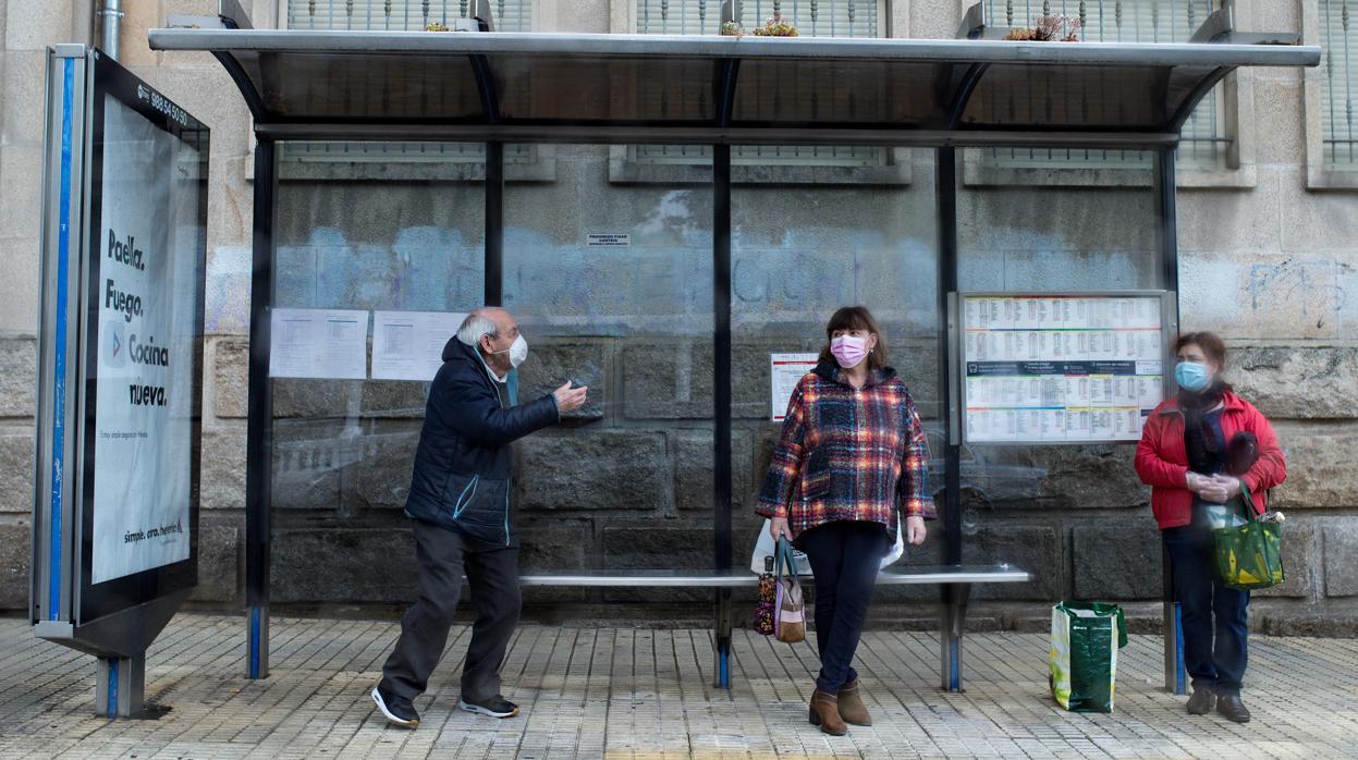 Personas protegidas con mascarillas esperan la llegada del autobús en una marquesina, este martes en Orense