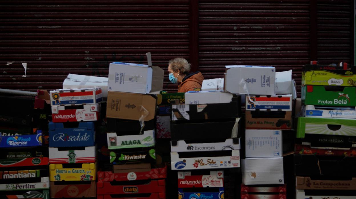 Una mujer con mascarilla camina junto a varias cajas de frutas y verduras en uno de los laterales de un mercado en La Coruña