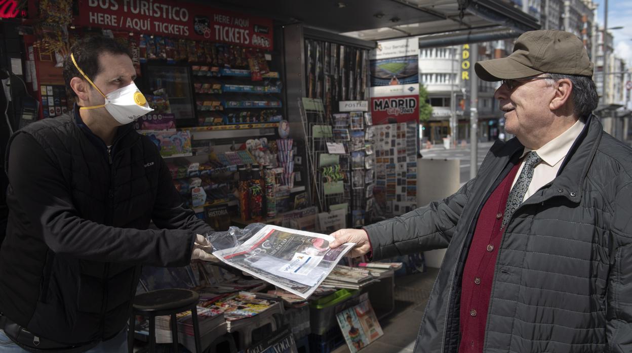 Un lector recoge su ejemplar de ABC en el quiosco, envuelto y con una mascarilla