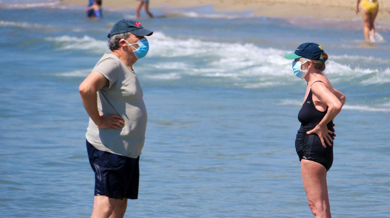 Imagen de dos personas con mascarilla en la playa del Postiguet de Alicante