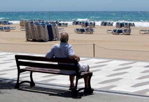 Un turista contempla la playa de Benidorm aún cerrada y con las hamacas apiladas