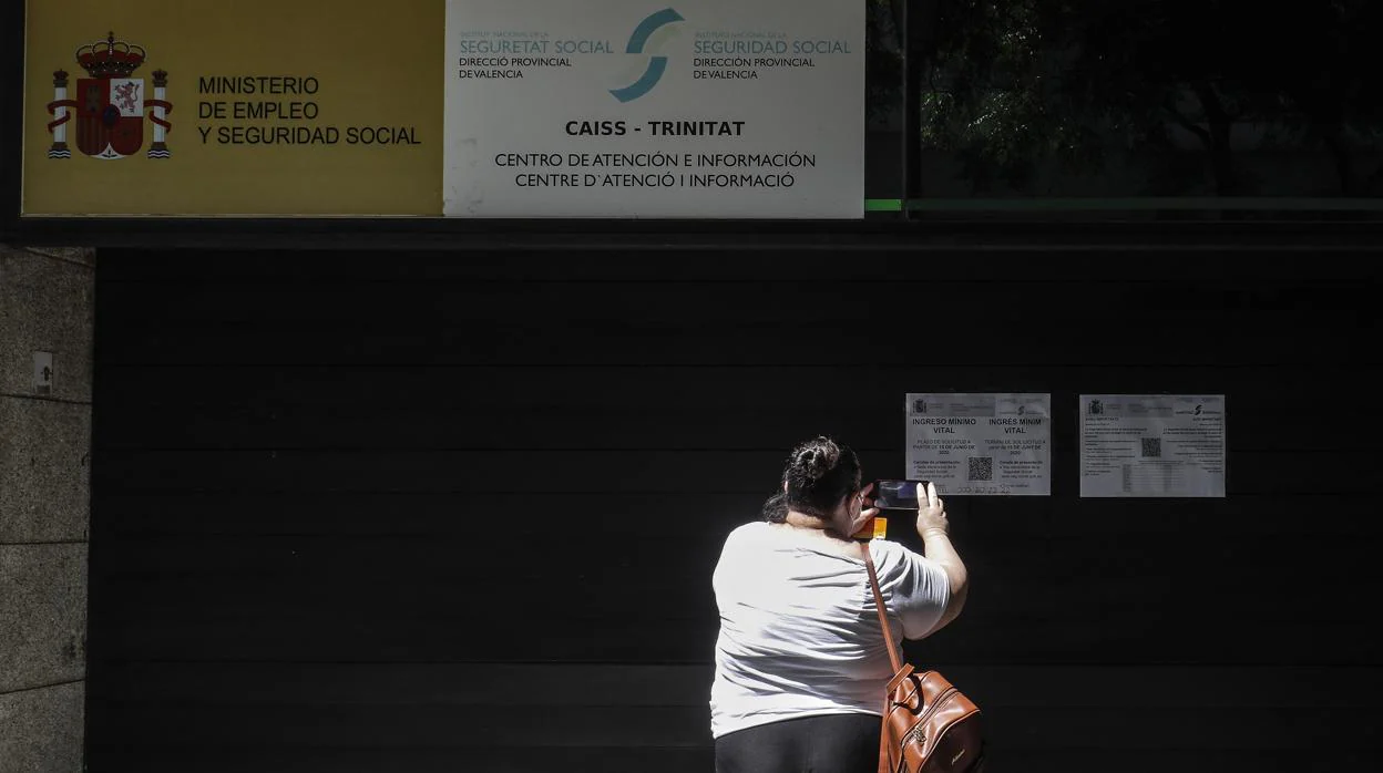 Una mujer fotografía este lunes el cartel de información sobre la solicitud del IMV en una oficina de Valencia