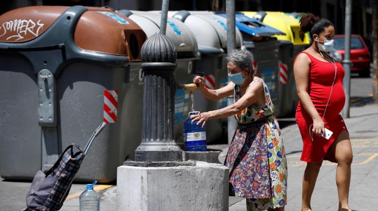 Una mujer llena una garrafa de agua en una fuente del barrio de La Torrassa de L'Hospitalet