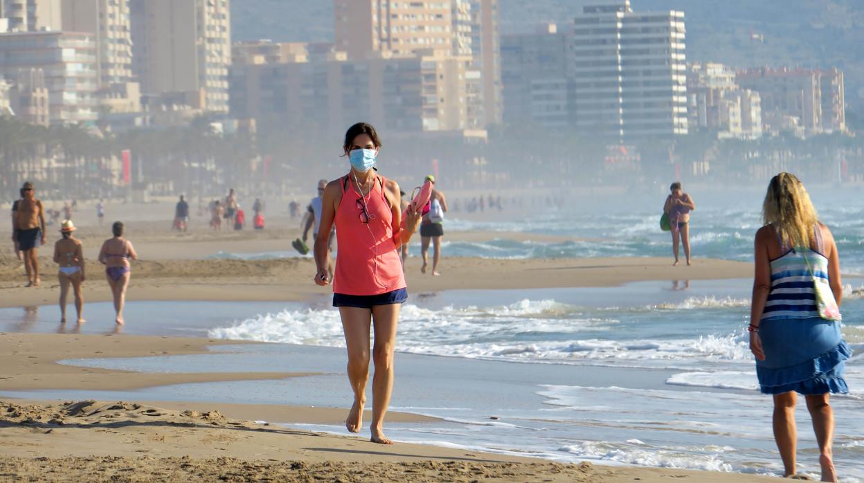 Imagen de una mujer paseando por la playa con mascarilla