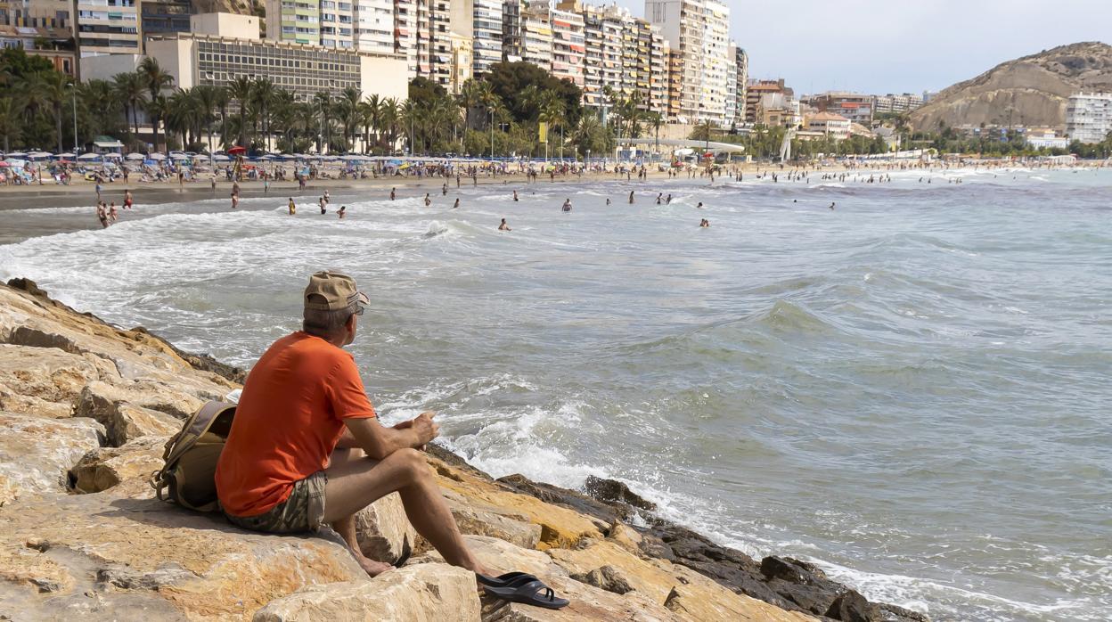 Imagen de un hombre observando a los bañistas en la playa del Postiguet (Alicante)