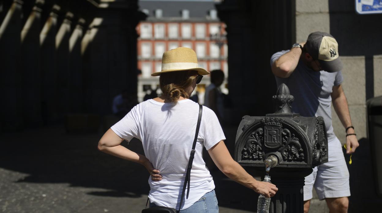 Una pareja de paseantes aguantan el calor en Plaza Mayor reponiendo agua en una fuente