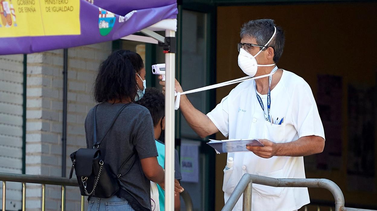 Un trabajador sanitario toma la temperatura a dos usuarios a su llegada al Centro de Salud de la localidad abulense de Candeleda, donde permanece un brote activo desde hace varios días