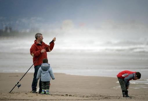 Un hombre con dos niños se prepara para pescar en la playa de la Malvarrosa