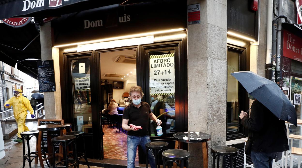 Un camarero desinfecta una mesa en el exterior de un bar