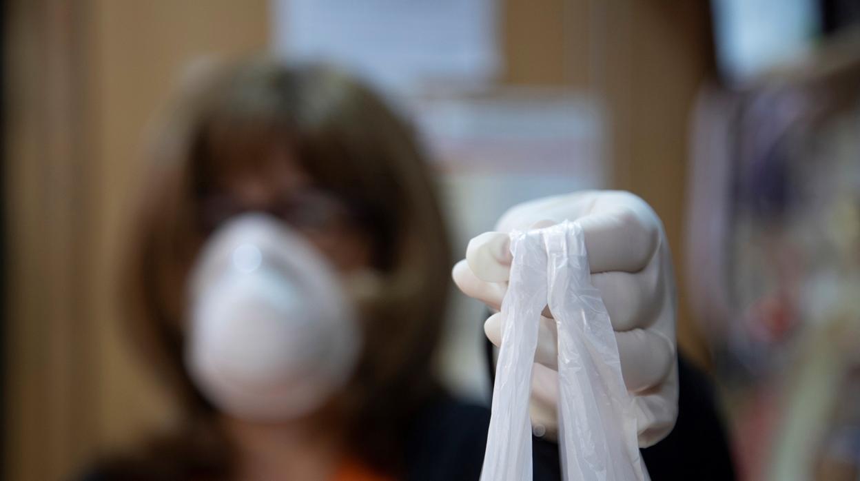 Imagen de una mujer con mascarilla y guantes y una bolsa de la compra