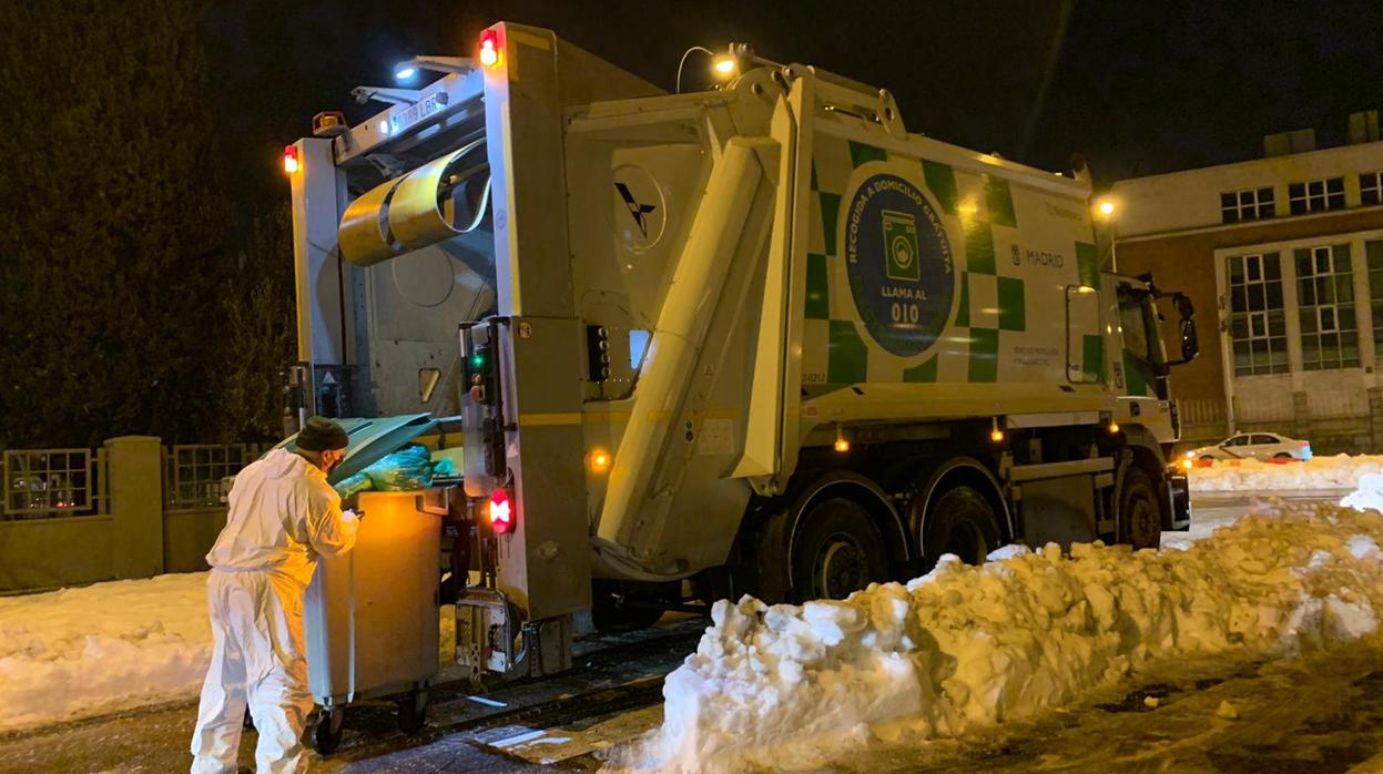 Un camión de la basura vacía los cubos en una calle de Madrid, rodeada por nieve