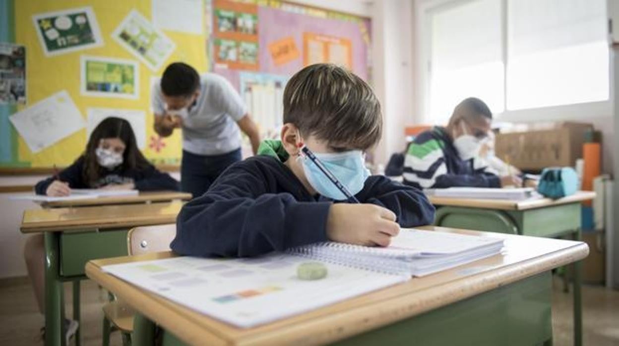 Un niño realiza sus deberes con la mascarilla puesta durante una clase