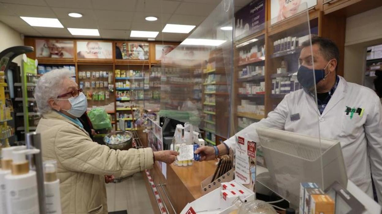 Un farmacéutico entrega a una usuaria la mascarilla FFP2 que regala la Comunidad de Madrid a los mayores de 65 años