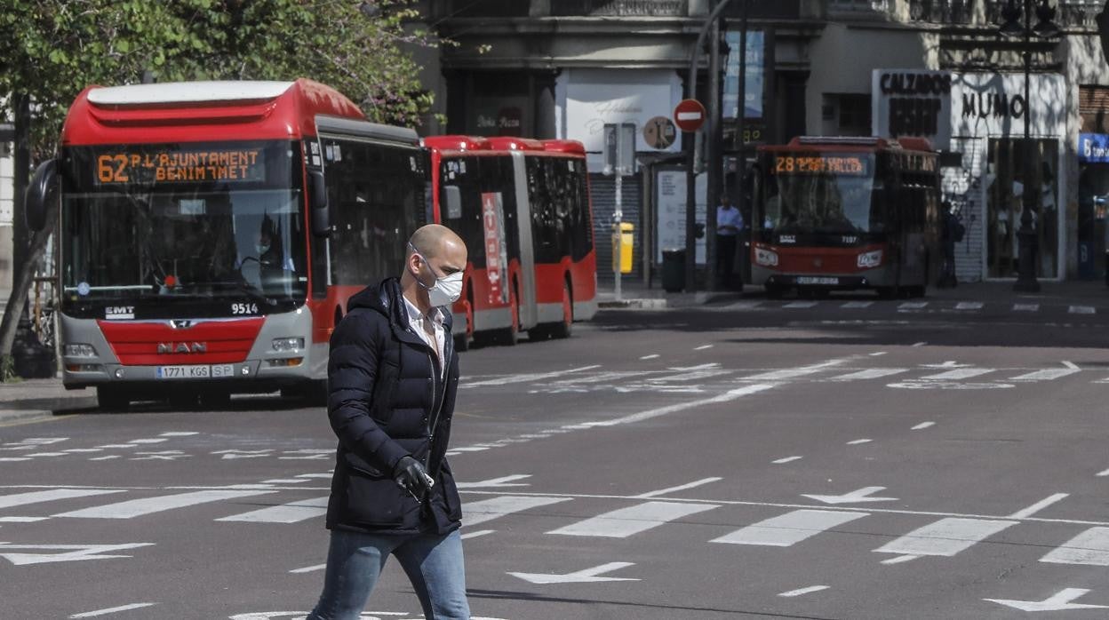 Imagen de un hombre cruzando por delante de dos autobuses de la EMT de Valencia