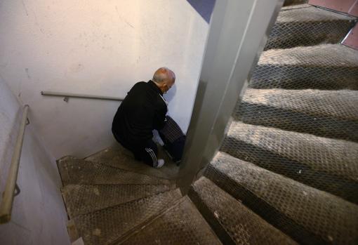 Un anciano sube el carro de la compra por la escalera de caracol, instalada hace año y medio, durante el cual la obra de instalación del ascensor ha estado parada