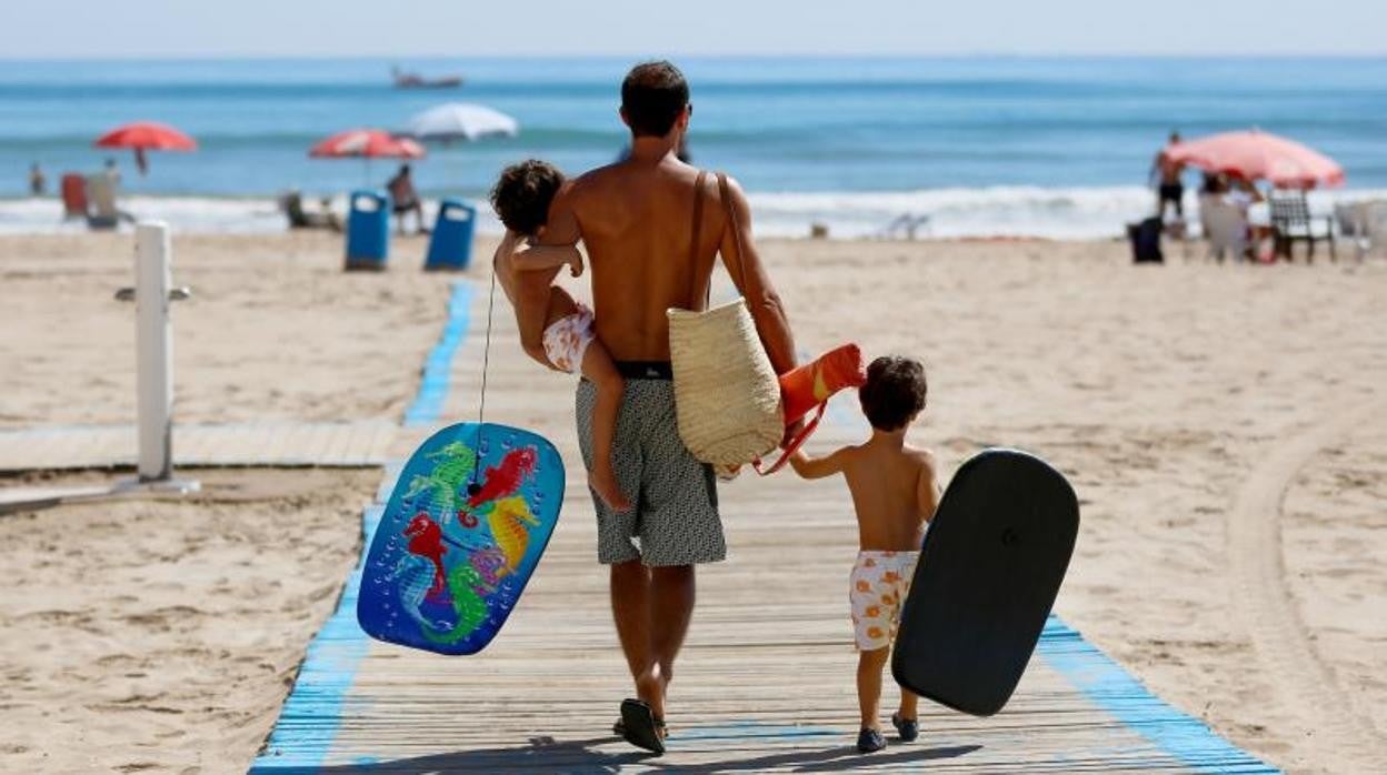 Un padre camina por la playa con sus dos hijos pequeños en Valencia