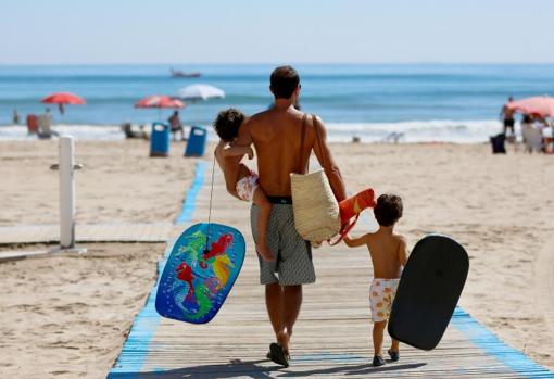 Un padre camina por la playa con sus dos hijos pequeños en Valencia