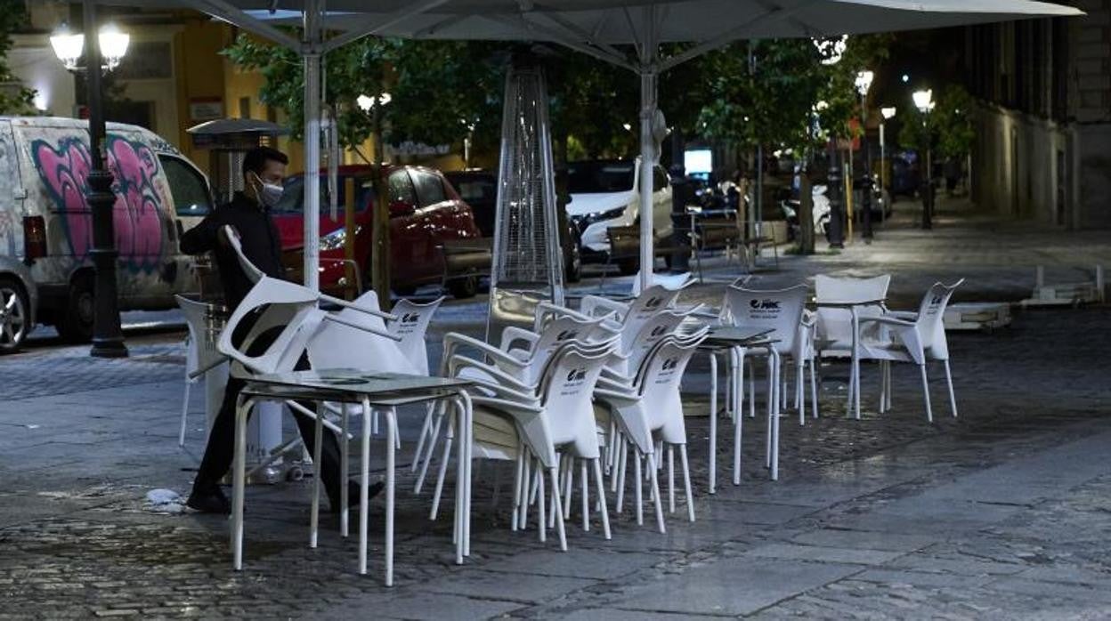 Un camarero recoge las sillasy las mesas de una terraza de Madrid