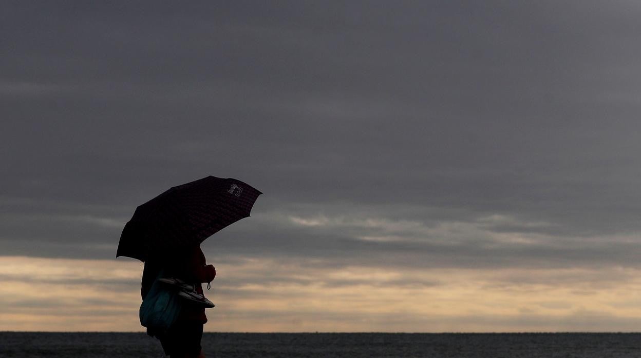 Imagen de archivo de una persona protegida de la lluvia con un paraguas en la playa de la Malvarrosa de Valencia