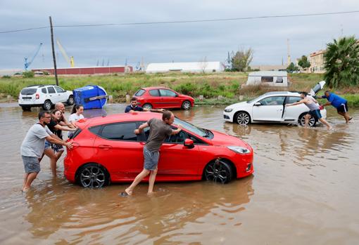 Imagen de varias personas arrastrando sus coches afectados por la lluvia