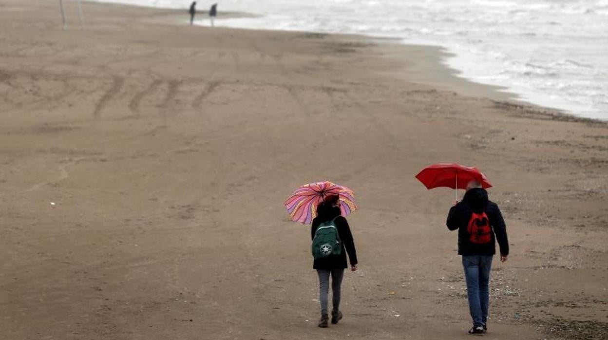 Paseantes con paraguas por una playa de Valencia, este fin de semana