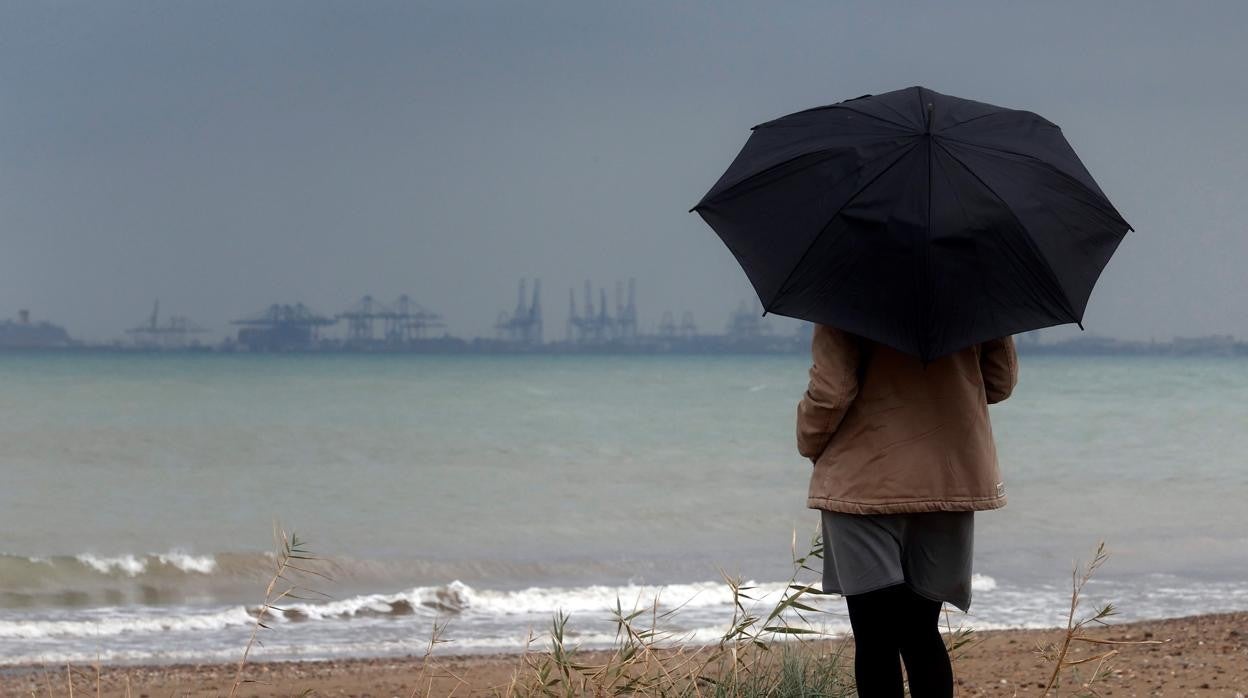 Imagen de una mujer contemplando el litoral brumoso y encapotado en Valencia