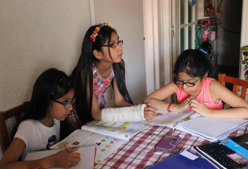 Tres menores hacen los deberes en casa acompañados de los auxiliares del Ayuntamiento de Madrid