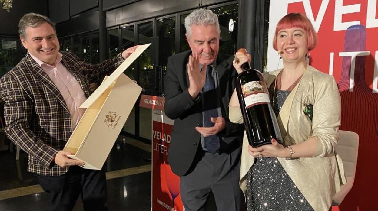 María Zaragoza recibe una botella de vino de la bodega Casa Cesilia de manos de Ezequiel Moltó (Vectalia), acompañada por el presentador de las Veladas Literarias de Maestral, Manuel Avilés