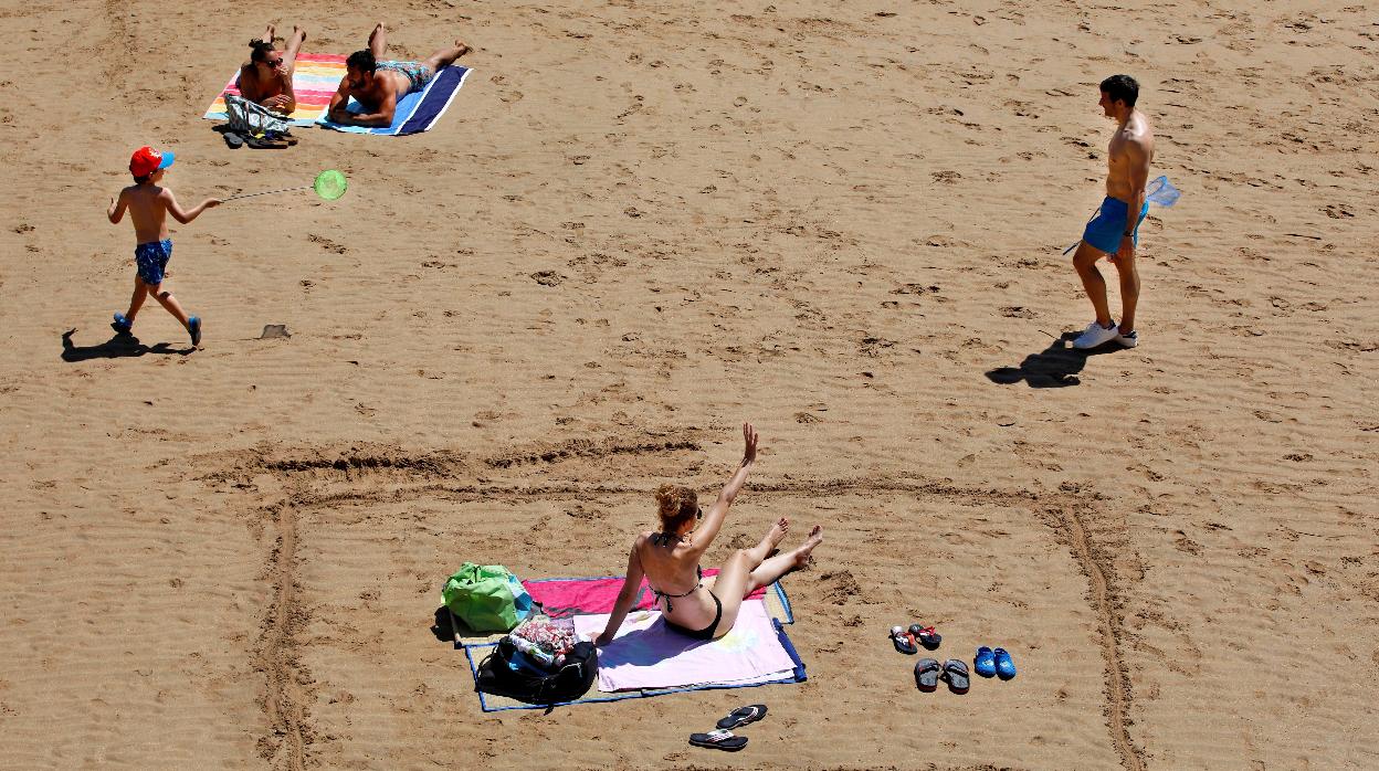Varias personas disfrutan de un soleado día de verano en la playa de San Lorenzo en Gijón, Asturias,