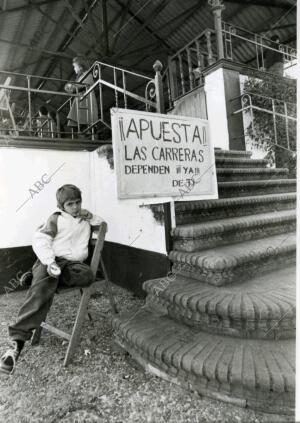 Un niño sentado junto a un cartel en el Hipódromo de Sevilla