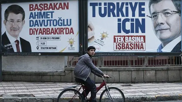 Un joven circula en bicicleta junto a dos carteles con la imagen del primer ministro turco, Ahmet Davutoglu, en Diyarbakir, Turquía,