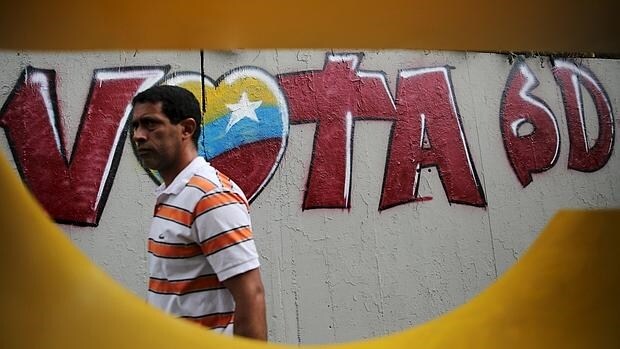 Un hombre pasa junto a una pintada que llama a votar en las legislativas del domingo, en una calle de Caracas