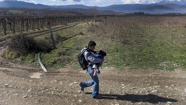 Un emigrante, que lleva un niño, cruza la frontera entre Grecia y Macedonia, cerca de la localidad de Gevgelija