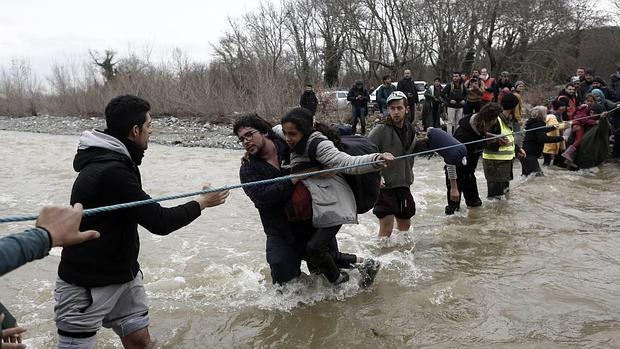 Un grupo de refugiados utiliza una cuerda para cruzar la frontera entre Grecia y Macedonia