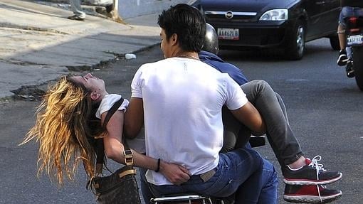 Dos hombres trasnportan en moto a una joven herida de bala en Valencia durante unas protestas contra el Gobierno