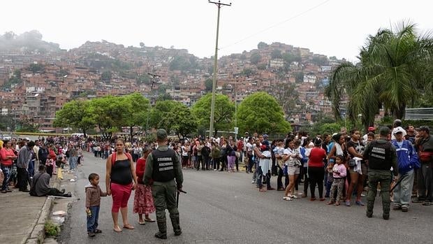 La Guardia Nacional Bolivariana vigila una larga cola de personas que esperan para comprar en un supermercado